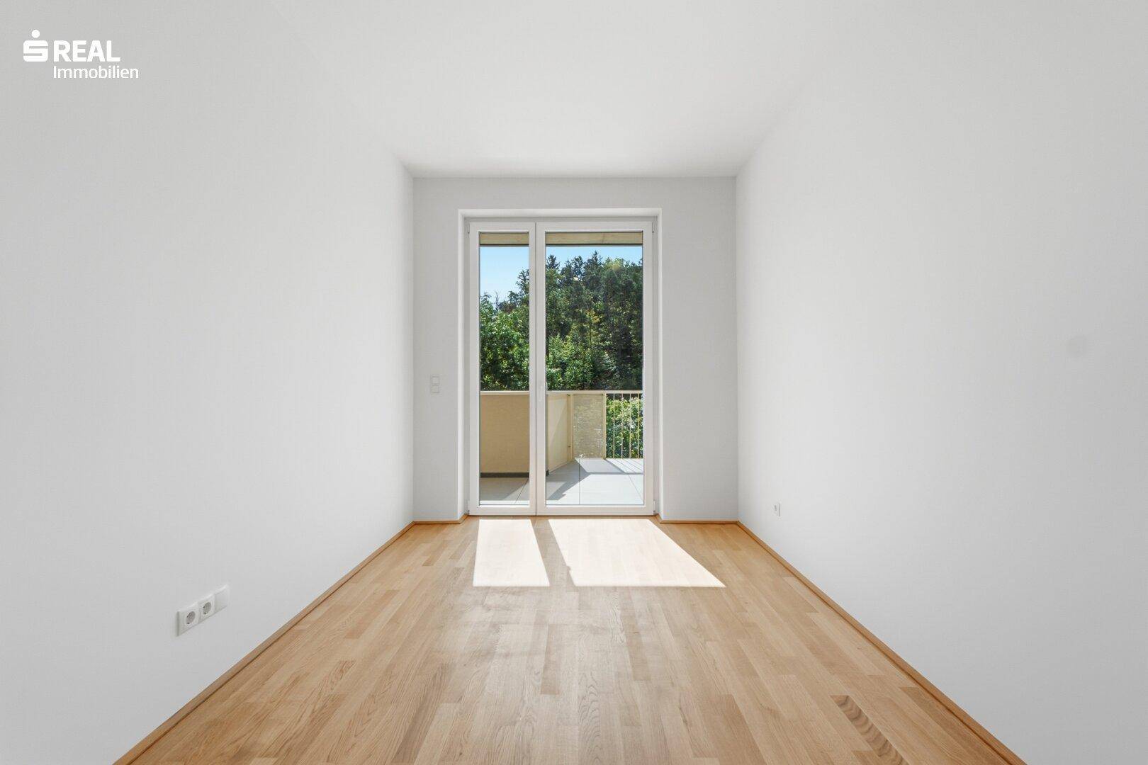 Helles Schlafzimmer mit Parkettboden und direktem Zugang zu einem kleinen Balkon.