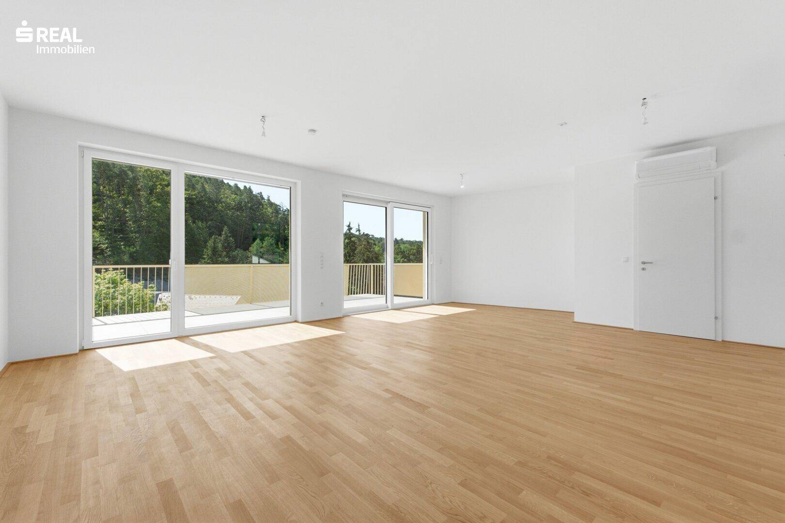 Geräumiges, helles Wohnzimmer mit Holzboden und Schiebetüren zum Außenbereich.