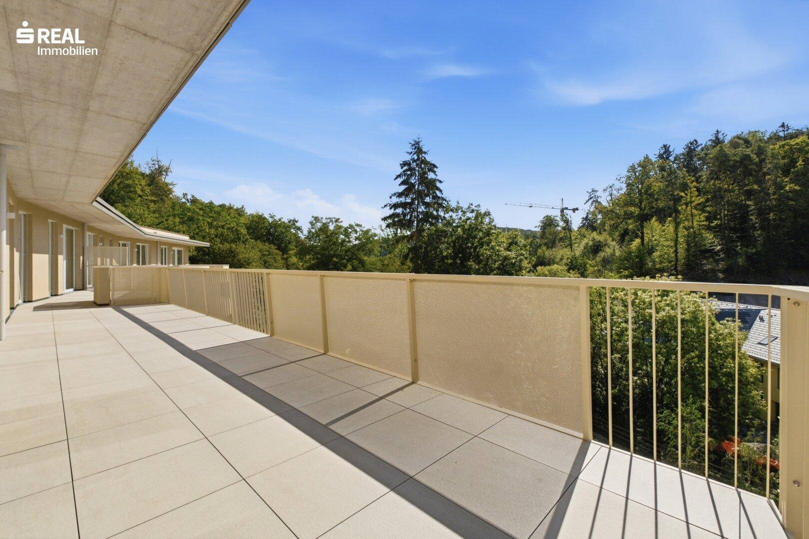 Großer, gefliester Balkon mit moderner Brüstung und weitem Blick ins Grüne.