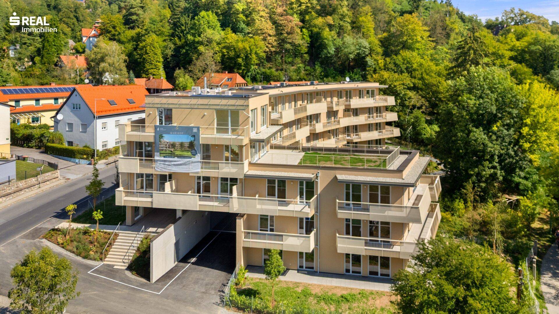 Ansicht der modernen Wohnanlage von oben mit gestaffelten Balkonen und begrüntem Flachdach in natürlicher Umgebung.