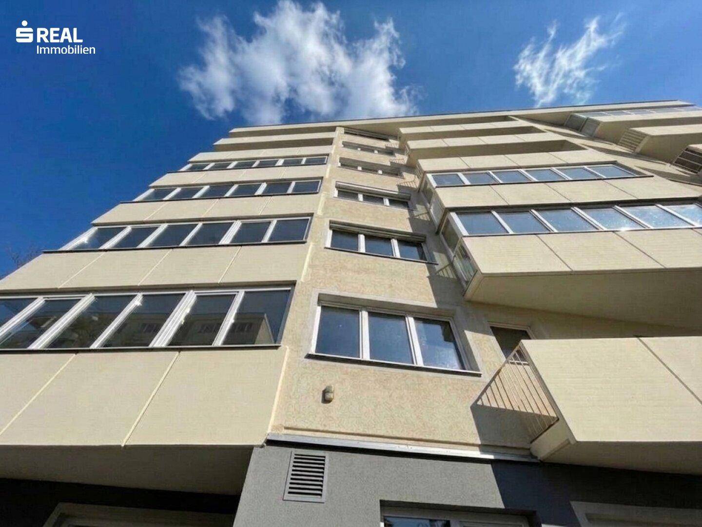 Moderne Fassade eines Mehrfamilienhauses mit gestuften Balkonen und vielen Fenstern unter blauem Himmel.