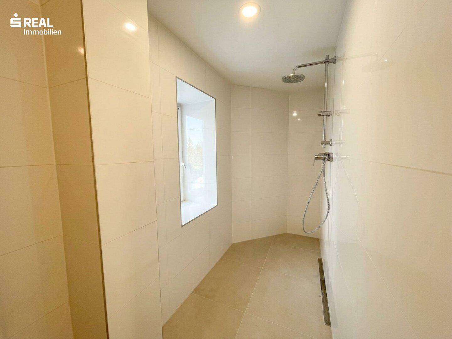 Modernes Badezimmer mit begehbarer Dusche, Regendusche und hellen Fliesen.