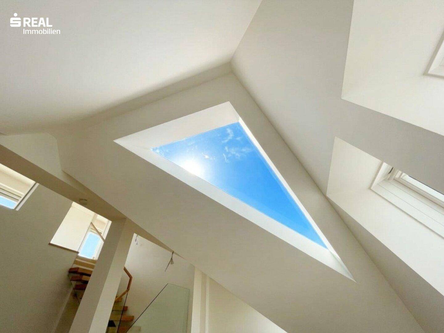 Großes dreieckiges Dachfenster lässt viel Sonnenlicht in den modernen Innenraum mit hohen Decken.