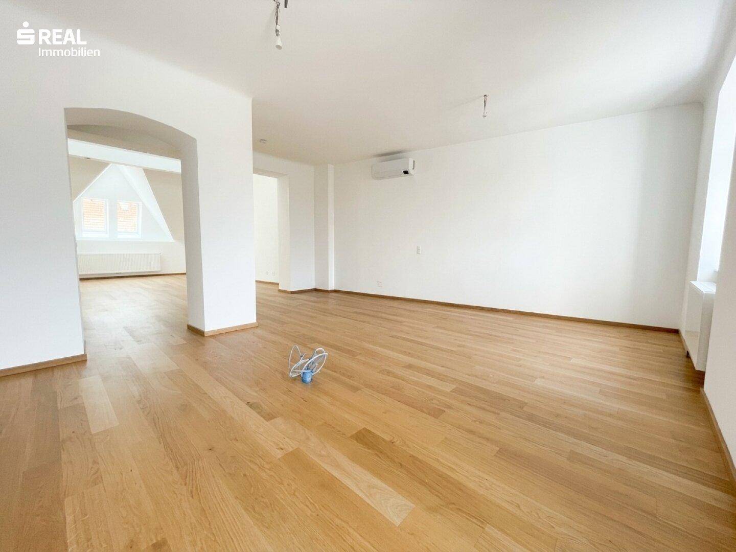 Heller, leerer Wohnraum mit Holzboden, weißen Wänden und Klimaanlage, bereit zum Einzug.