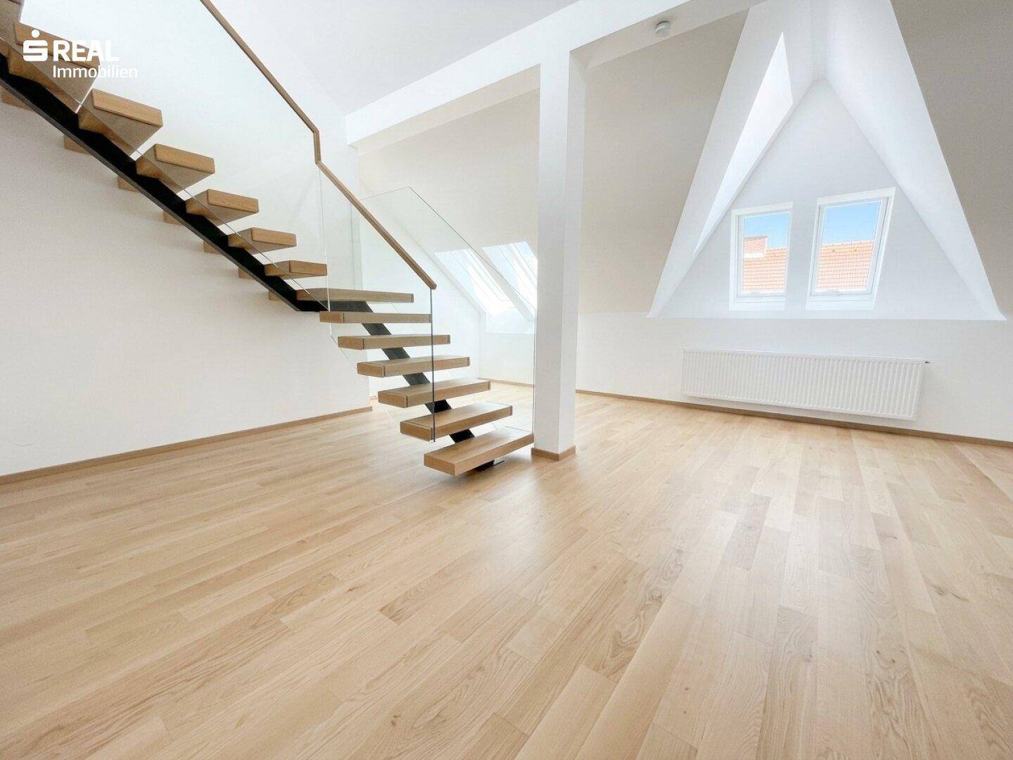 Offener Raum im Dachgeschoss mit moderner Holztreppe, Holzboden und Dachfenstern für viel Licht.