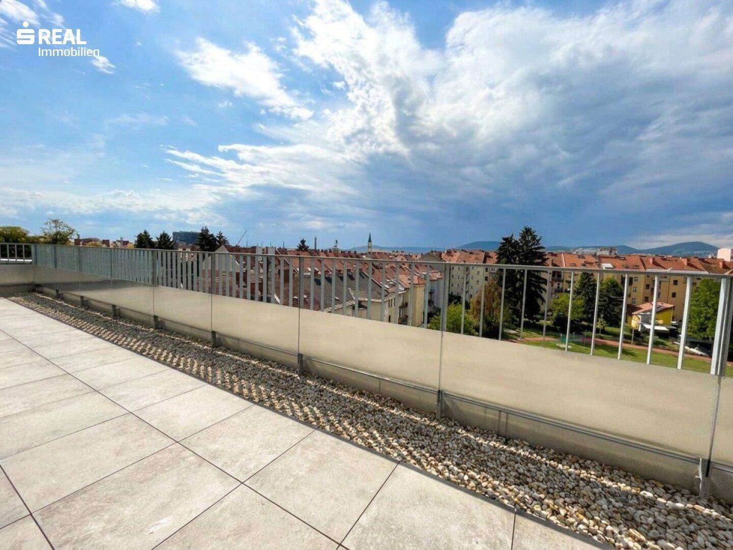 Weitläufige Dachterrasse mit moderner Glasbrüstung und Panoramablick über die Dächer der Stadt.