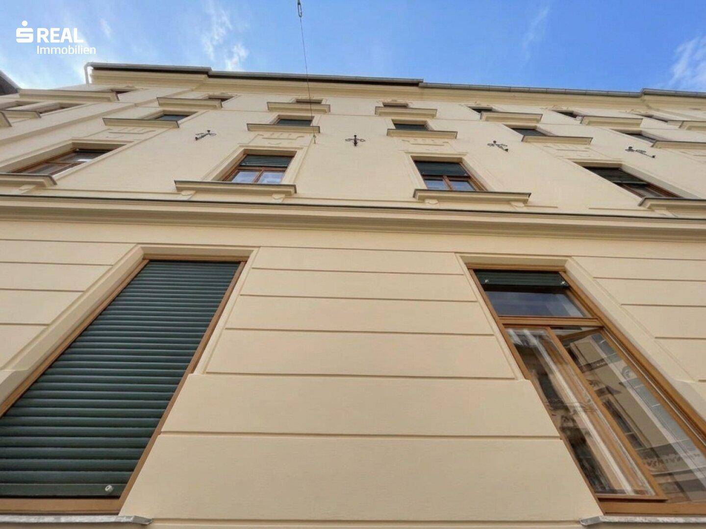 Detailansicht der historischen Gebäudefassade mit Fenstern, Rollläden und Putzornamenten.