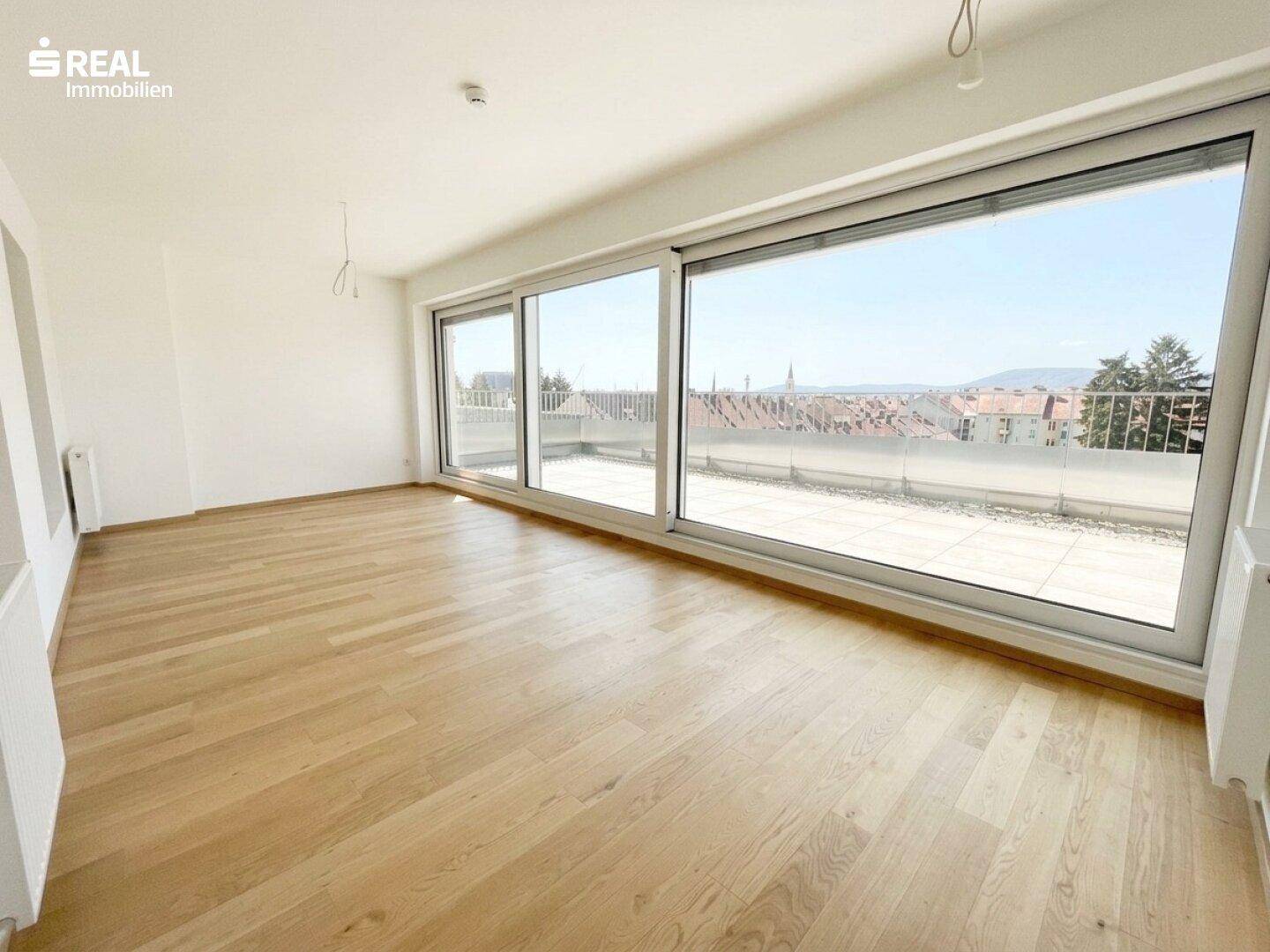 Heller Wohnraum mit großen Schiebefenstern und Zugang zu einer Terrasse mit Stadtblick.