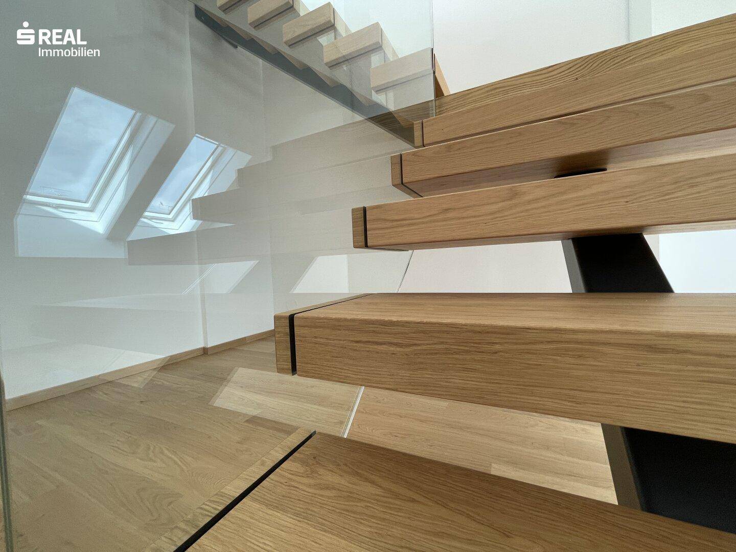 Moderne Holztreppe mit Glasgeländer und natürlichem Lichteinfall durch Dachfenster.