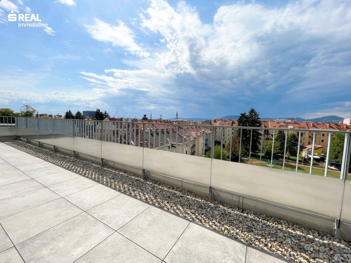 Weitläufige Dachterrasse mit modernem Glasgeländer und Panoramablick auf die umliegende Stadtlandschaft.