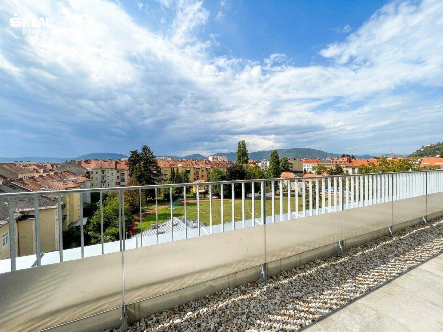 Geräumige Dachterrasse mit Kiesstreifen und einem weiten Blick über die Dächer der Stadt und grüne Hügel.