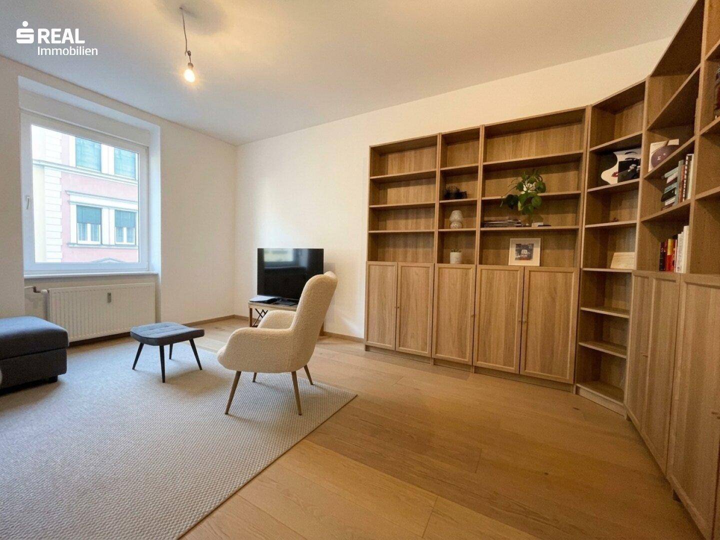 Helles Wohnzimmer mit großem Bücherregal aus Holz und Parkettboden.
