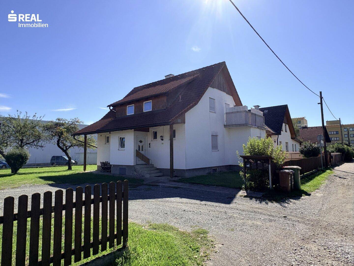 Gesamtansicht des Hauses mit Kiesauffahrt, Holzzaun und angrenzender Nachbarschaft unter blauem Himmel.