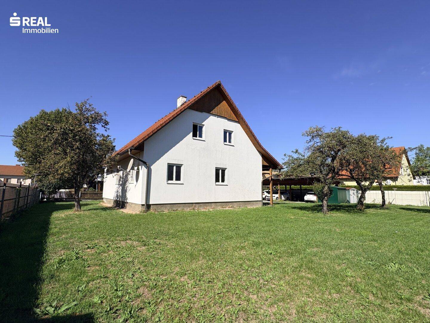 Weißes Einfamilienhaus mit rotem Ziegeldach, umgeben von einem gepflegten grünen Rasen und Bäumen.