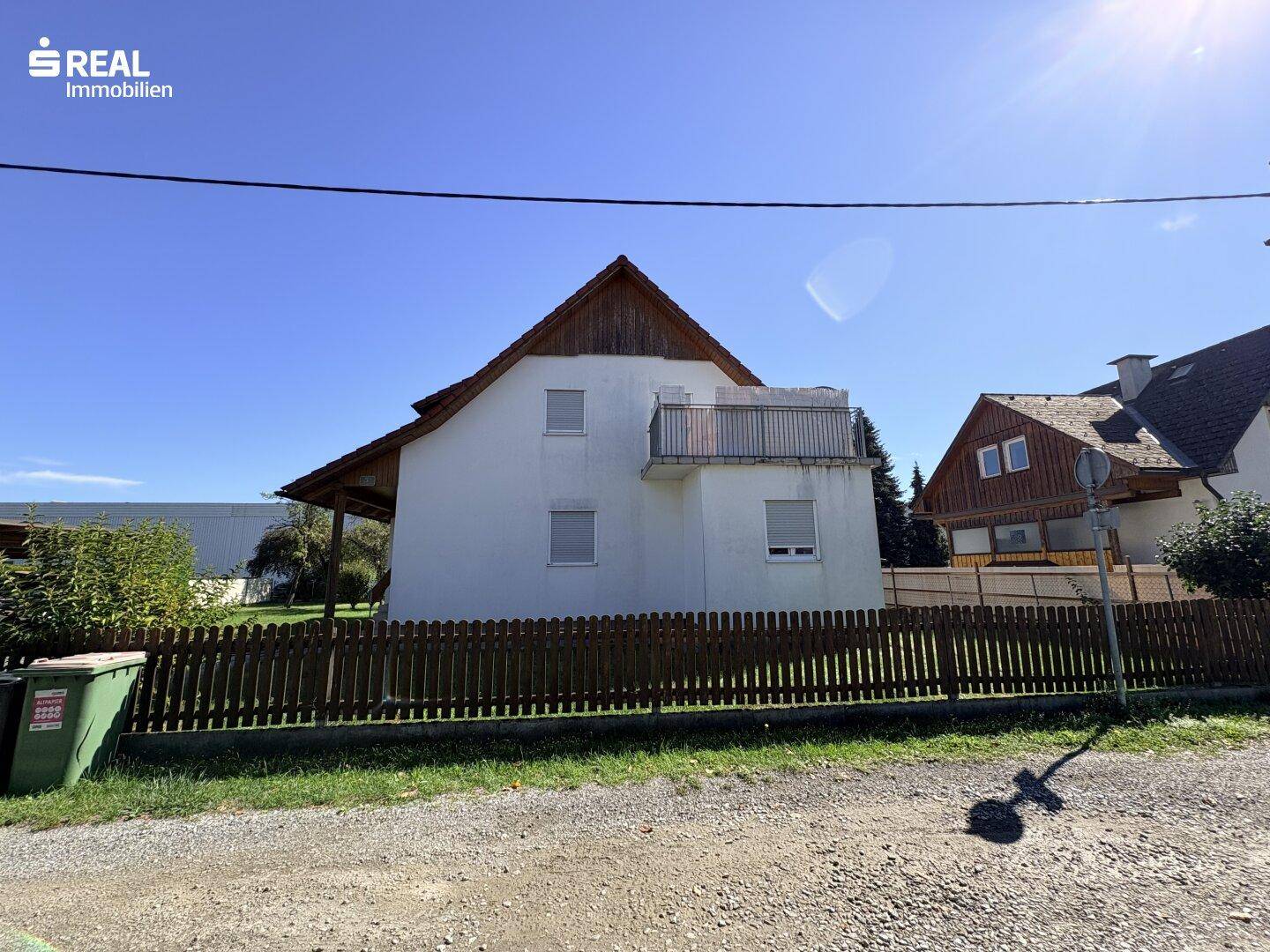 Seitenansicht des Hauses mit kleinem Balkon, Holzzaun und sonnigem Wetter.