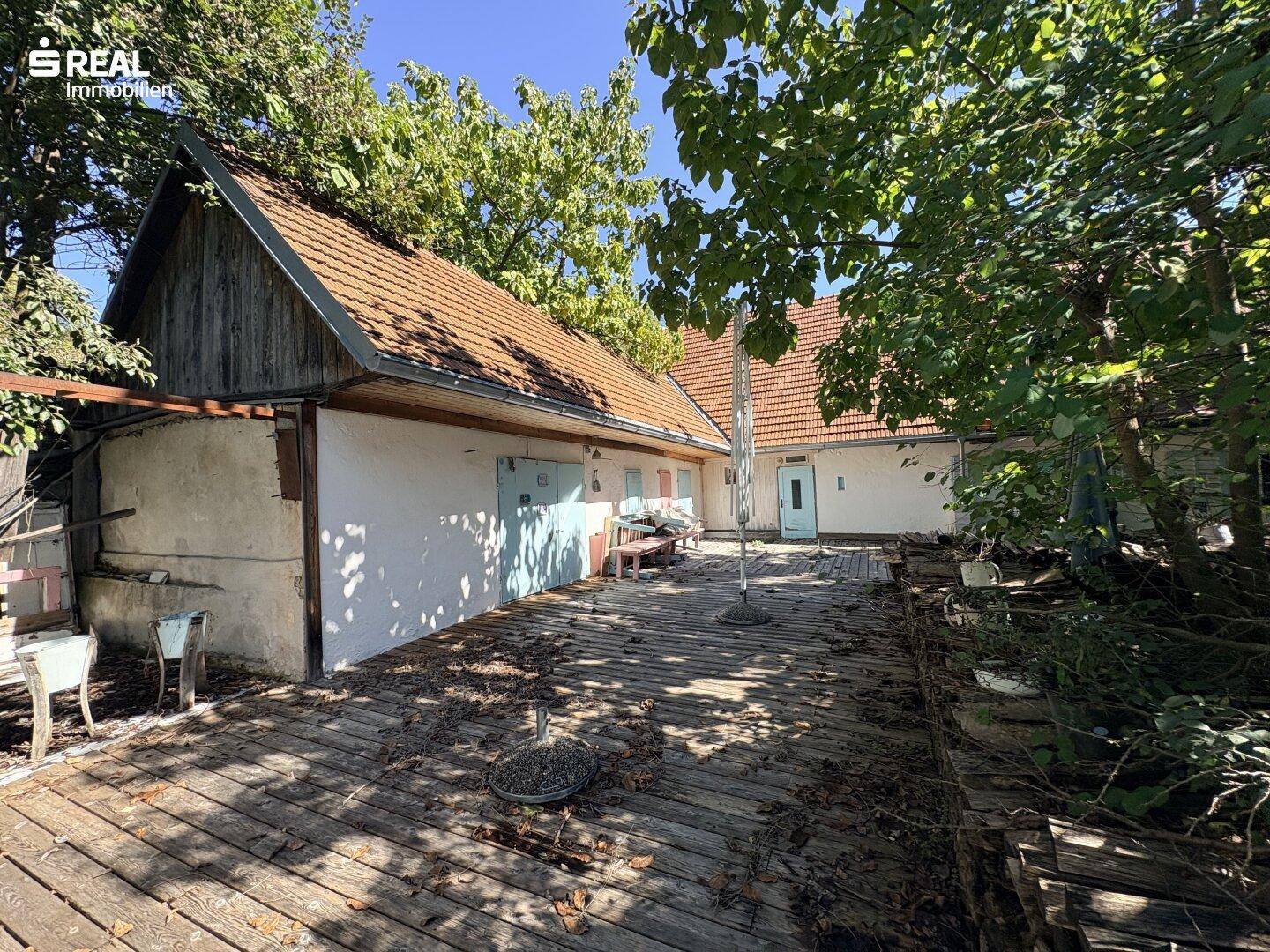 Weitläufige Holzterrasse mit angrenzenden Nebengebäuden und viel Potenzial für Gestaltung.