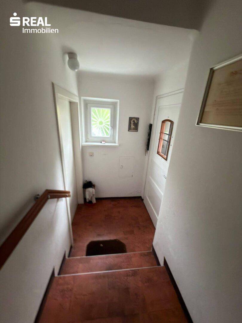 Eingangsbereich mit Treppe, Fenster und einer Tür, die in den Wohnbereich führt.