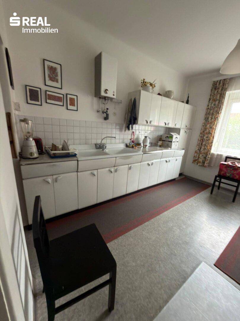 Einfache Küche mit weißen Schränken, Spüle und Fenster, ausgestattet mit grundlegenden Geräten.