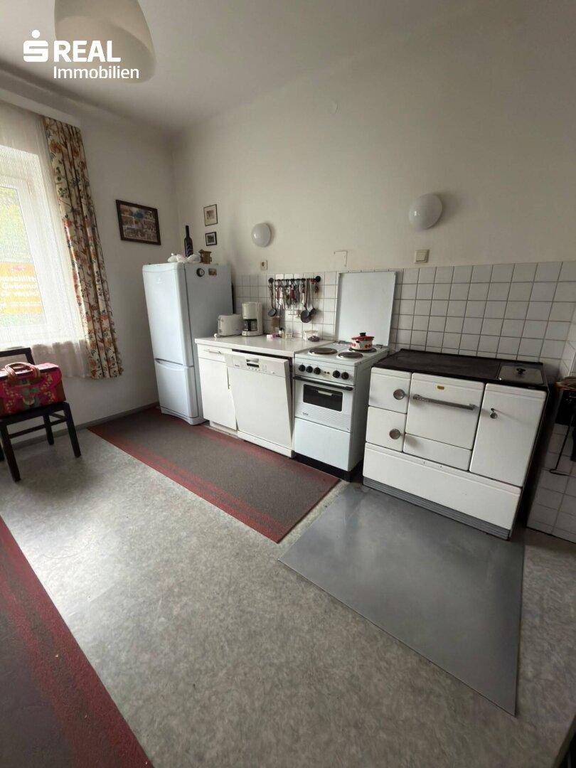 Funktionale Küche mit älteren Geräten wie Kühlschrank, Herd und Spülmaschine.