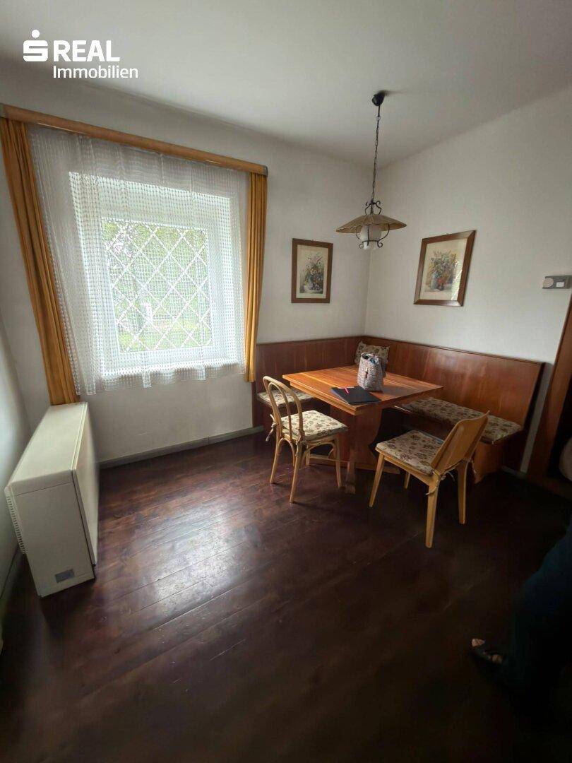 Gemütlicher Essbereich mit Eckbank, Holztisch und Stühlen neben einem Fenster.