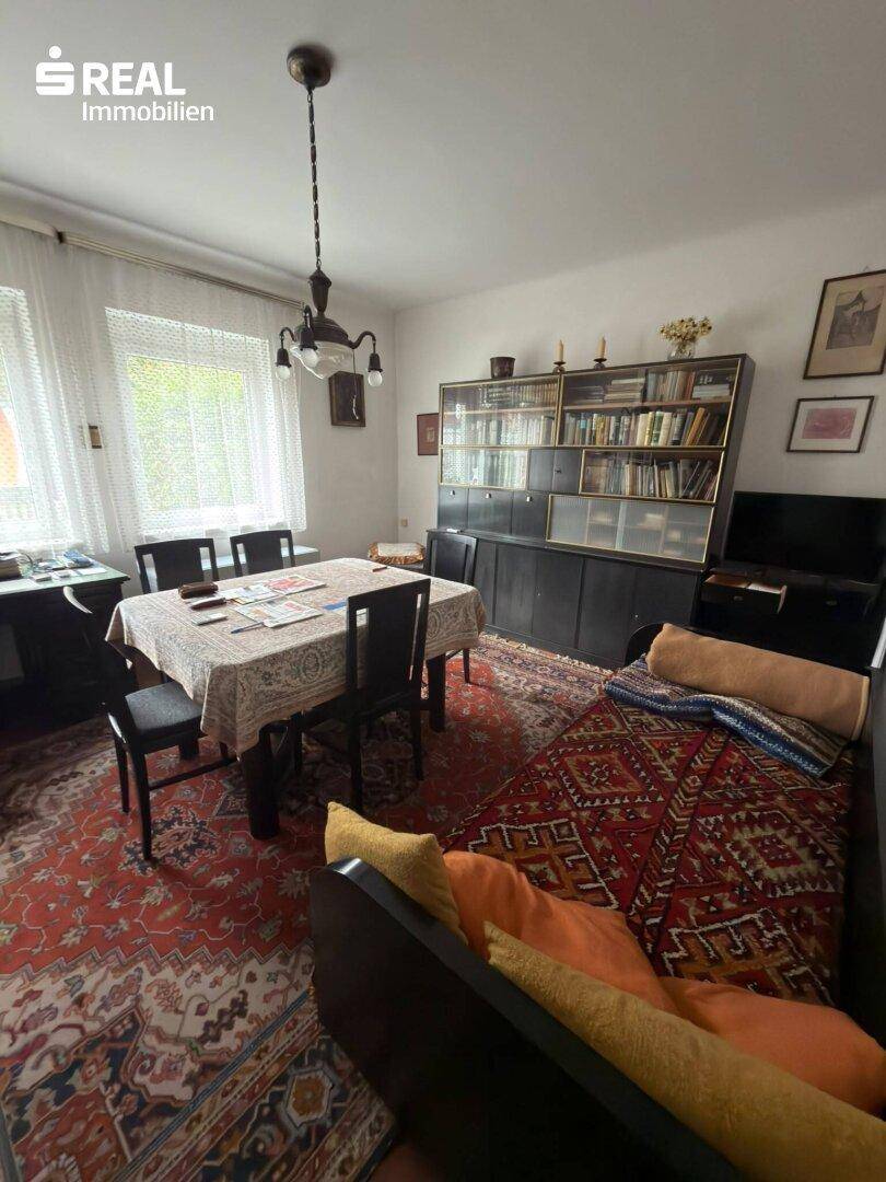 Wohn- und Essbereich mit Bücherregal, Esstisch und einem Sofa, dekoriert mit Teppichen.