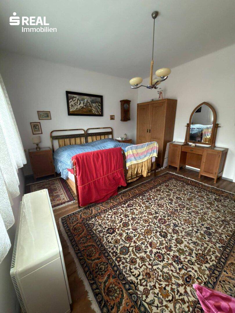 Schlafzimmer mit Doppelbett, Teppich, Holzmöbeln und einem Fenster für natürliches Licht.