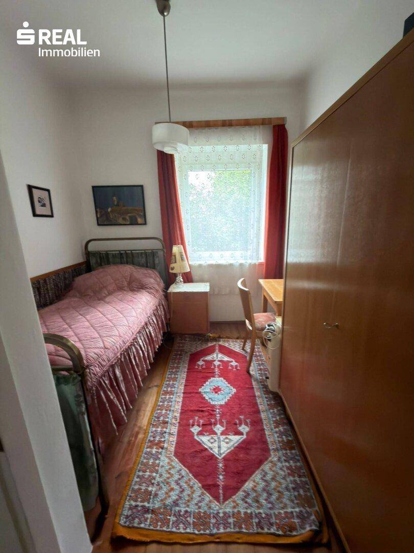 Kleines Schlafzimmer mit Einzelbett, Schrank und Schreibtisch am Fenster.