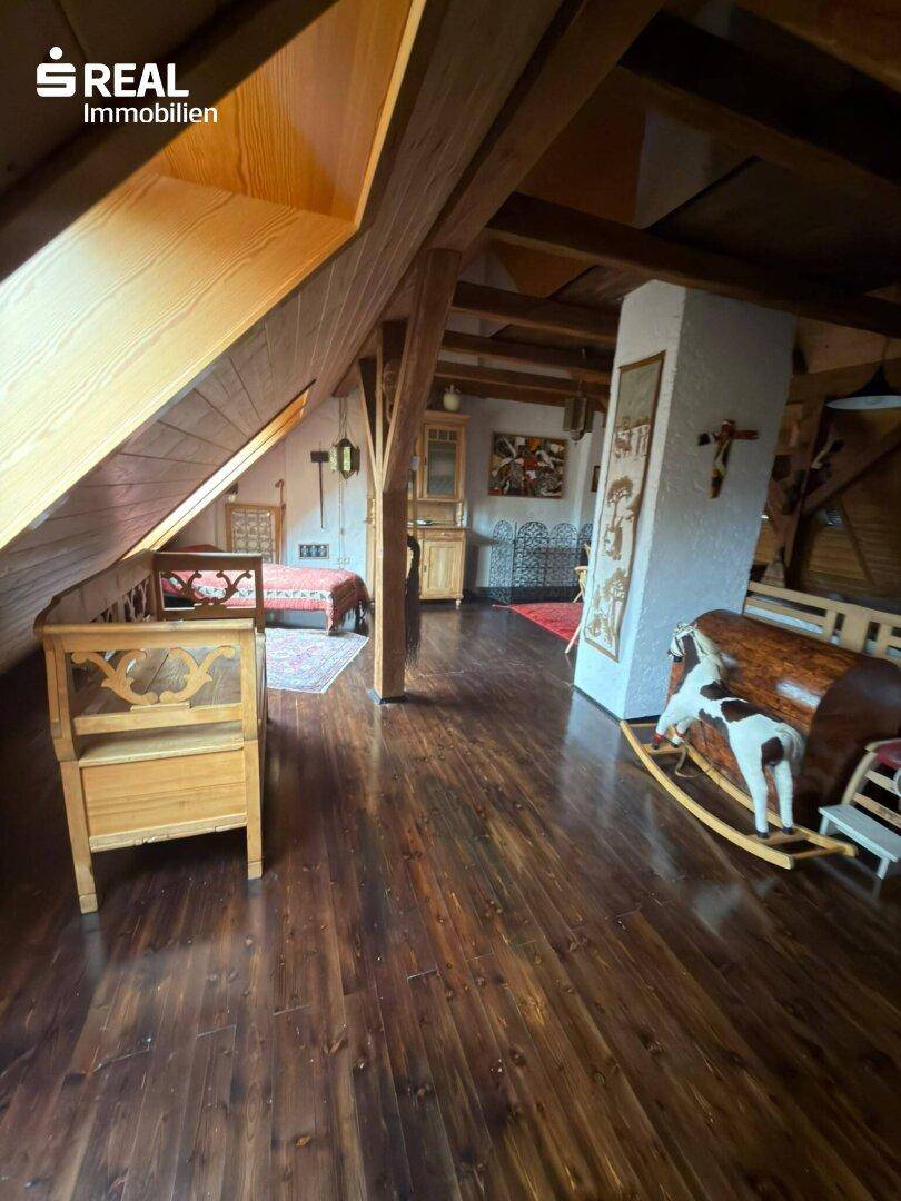 Ausgebauter Dachboden mit Holzbalken, Holzboden und rustikalen Möbeln, als Wohnraum genutzt.