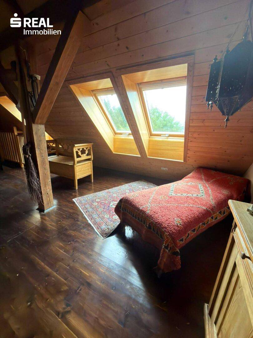 Gemütliches Schlafzimmer im Dachgeschoss mit Holzbalken, Holzverkleidung und Dachfenstern für natürliches Licht.