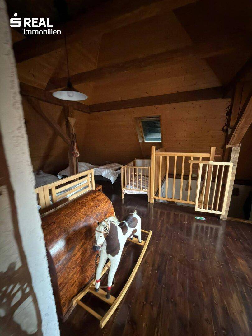 Rustikales Kinderzimmer im Dachgeschoss mit Holzbalken, Holzverkleidung und Spielzeug für eine warme Atmosphäre.