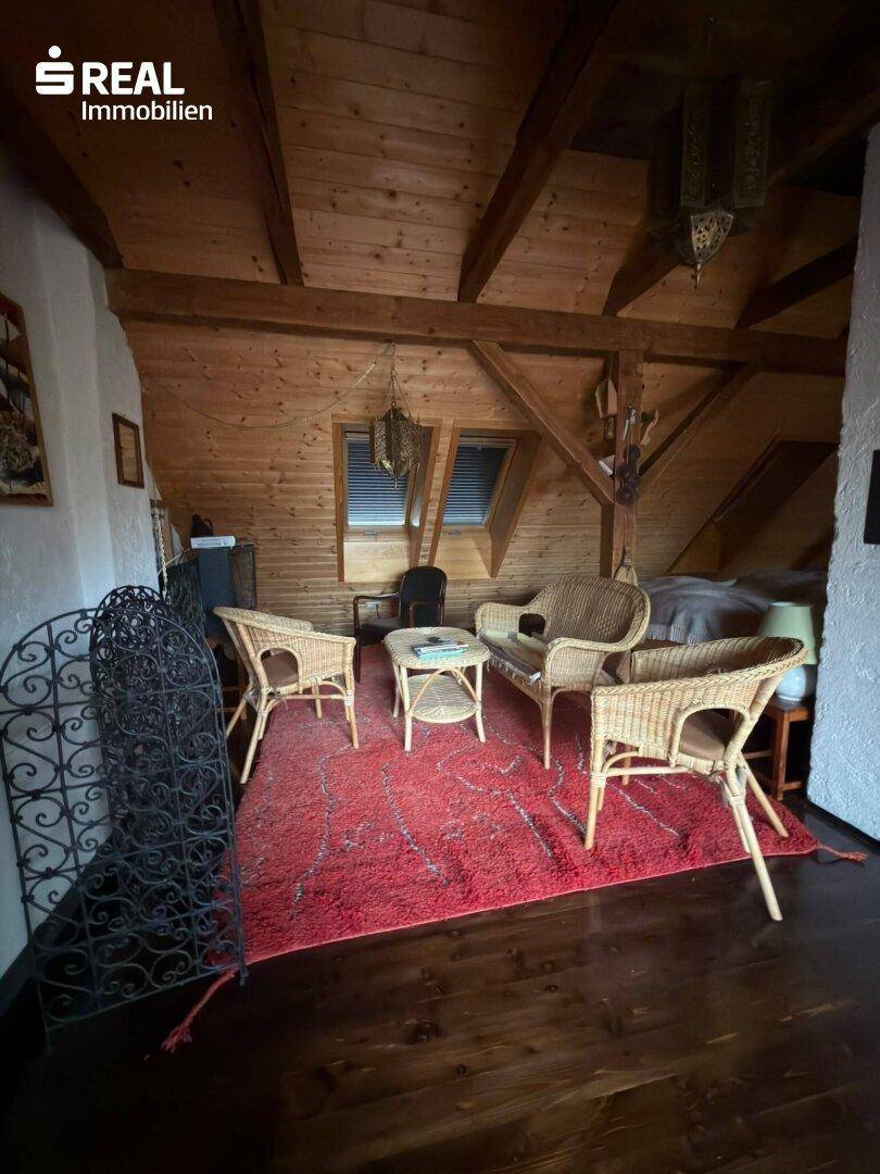 Wohnbereich im Dachgeschoss mit Korbmöbeln, Holzbalken und rustikaler Dekoration, ideal zum Entspannen.