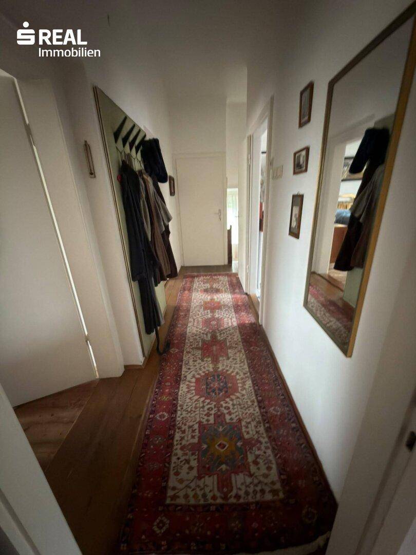 Langer Flur mit Teppichläufer, Garderobe und Spiegel, der zu den Zimmern führt.