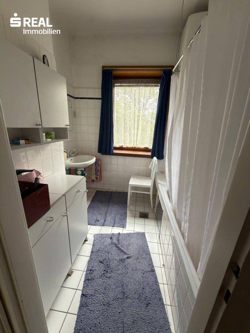 Funktionales Badezimmer mit weißen Fliesen, Waschbecken und Duschvorhang, hell durch das Fenster.