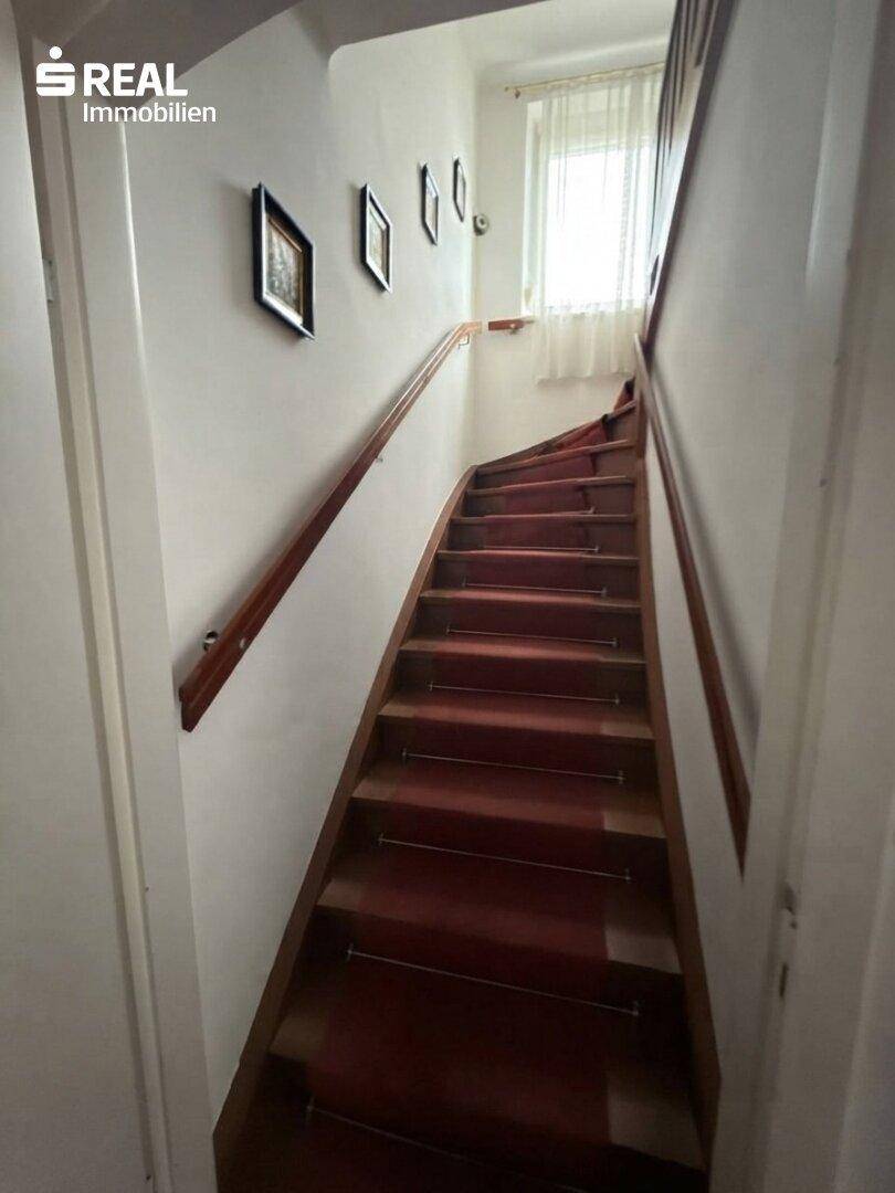Holztreppe mit Teppichläufer und Handlauf, die in die obere Etage führt.