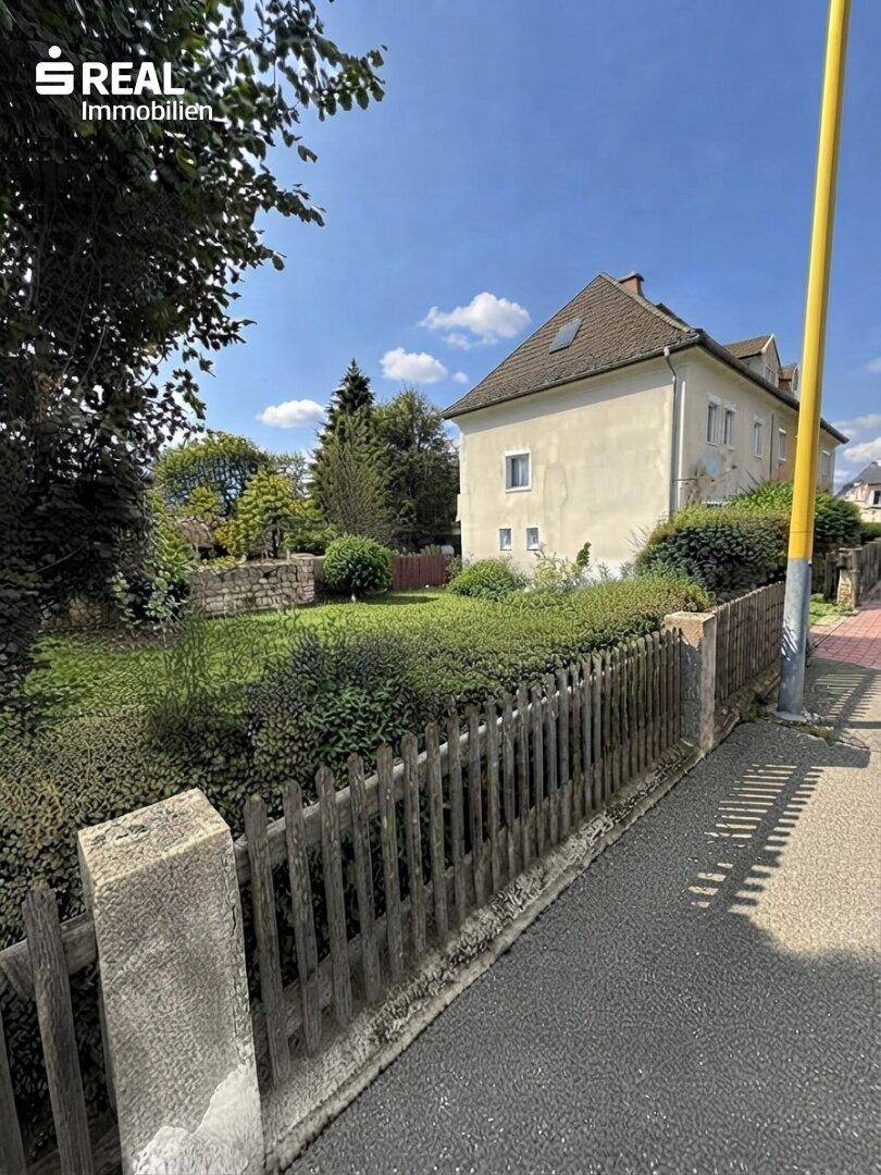 Seitenansicht des Hauses mit großem Gartenbereich und altem Holzzaun unter blauem Himmel.