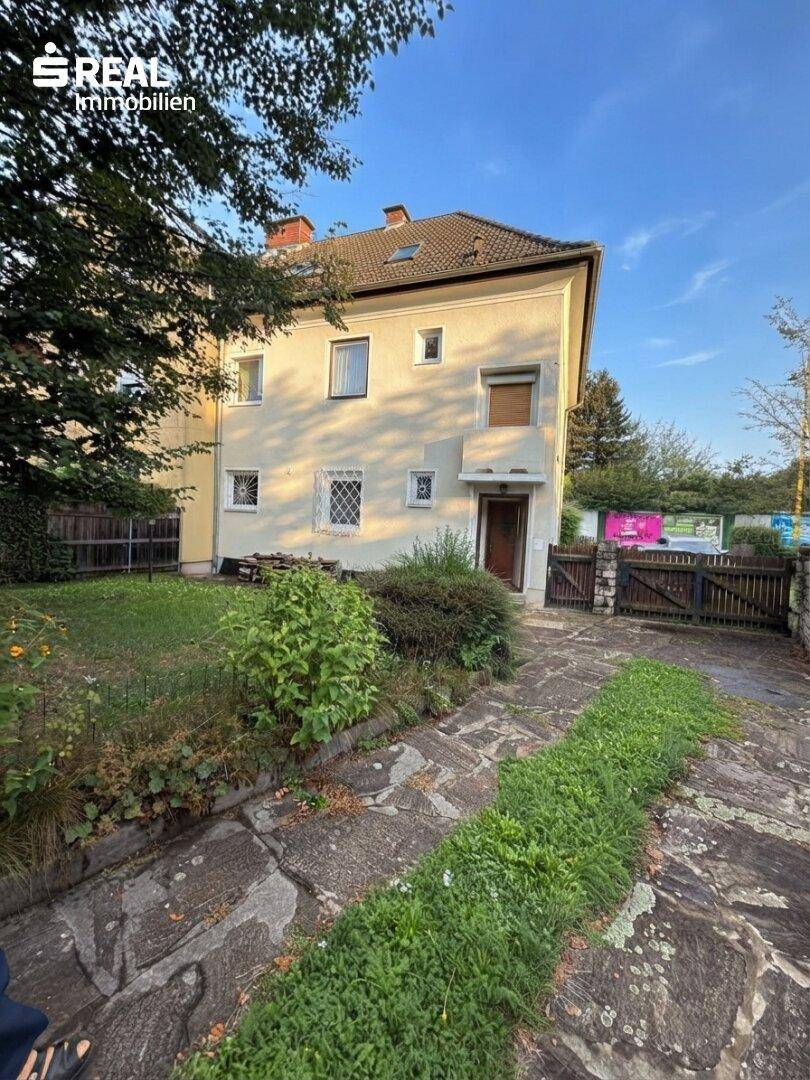 Vorderansicht des Hauses mit gepflasterter Auffahrt und grünem Gartenbereich bei Sonnenschein.