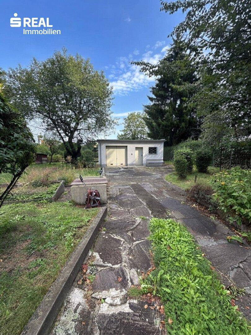 Garage im hinteren Gartenbereich mit gepflasterter Zufahrt und umgebender Grünfläche.