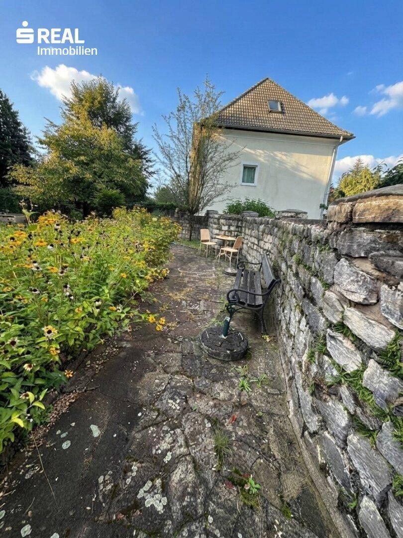 Rustikale Steinterrasse mit Sitzgelegenheiten und einer Steinmauer im Gartenbereich.
