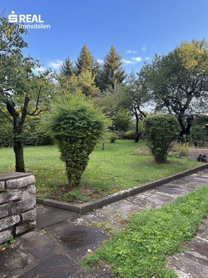 Gartenweg mit gepflegten Sträuchern und Bäumen, der zu weiteren Gartenbereichen führt.