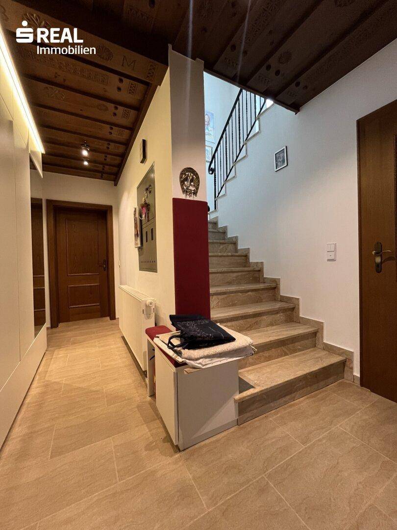 Geräumiger Flur mit Holzbalkendecke, Steinfliesenboden und einer eleganten Treppe.