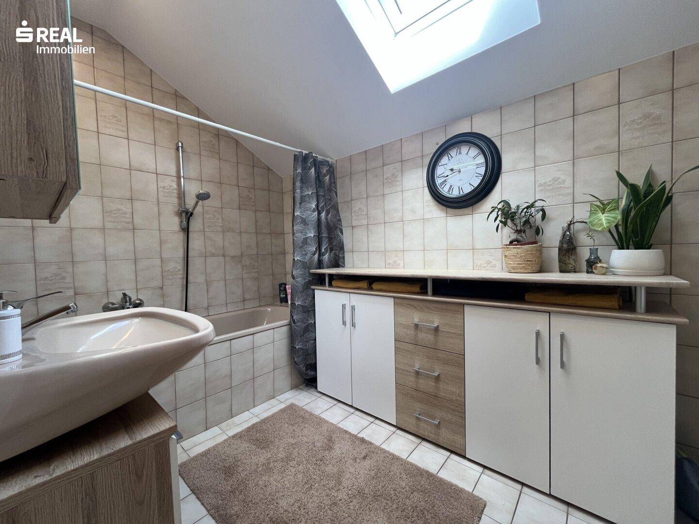 Badezimmer mit Badewanne, Duschvorhang, Waschtisch und Oberlicht für natürliches Licht.