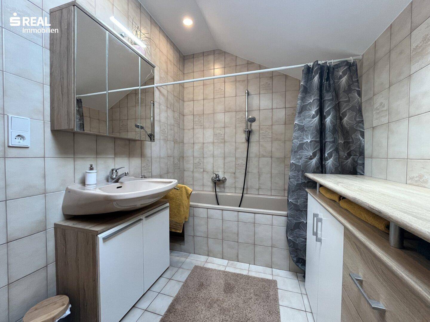 Funktionales Badezimmer mit Badewanne, Duschvorrichtung und Spiegelschrank über dem Waschtisch.