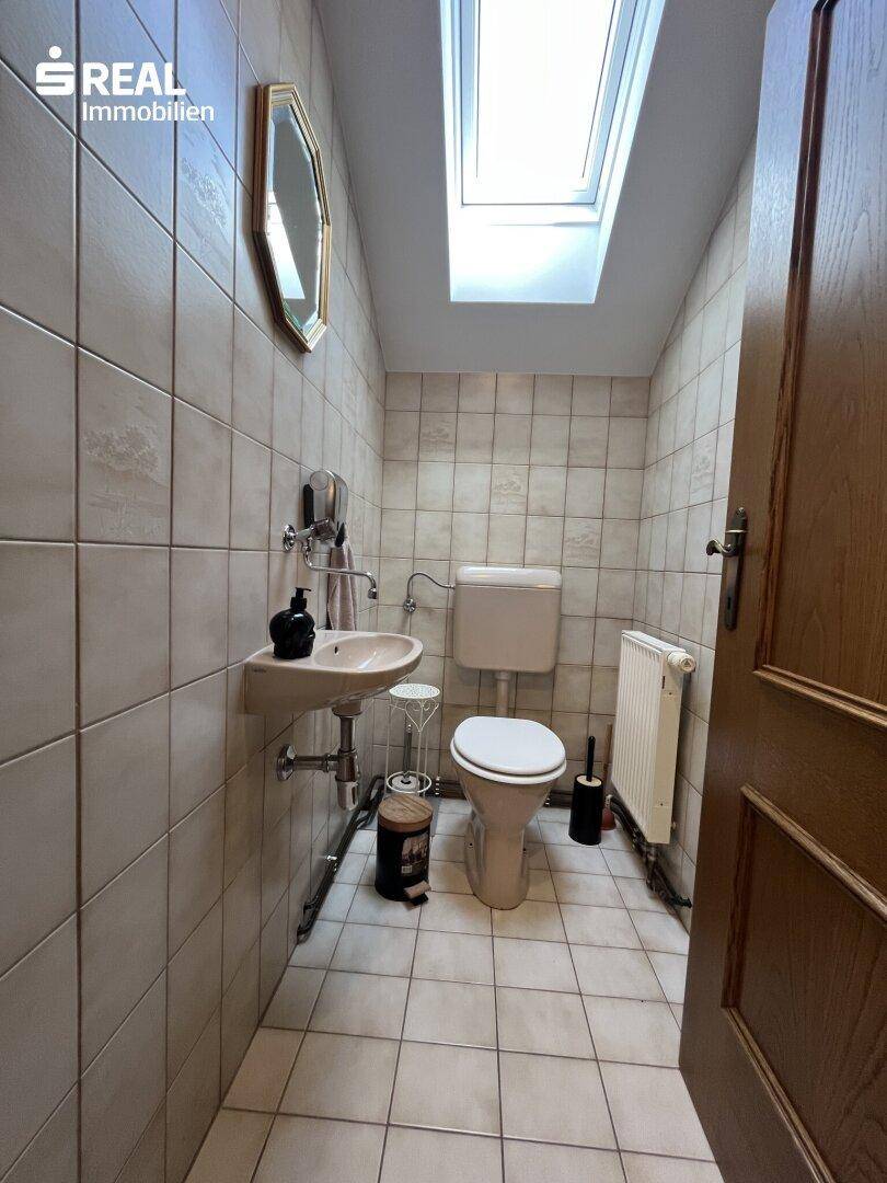 Kleines Gäste-WC mit Toilette, Handwaschbecken und einem Oberlicht für Tageslicht.