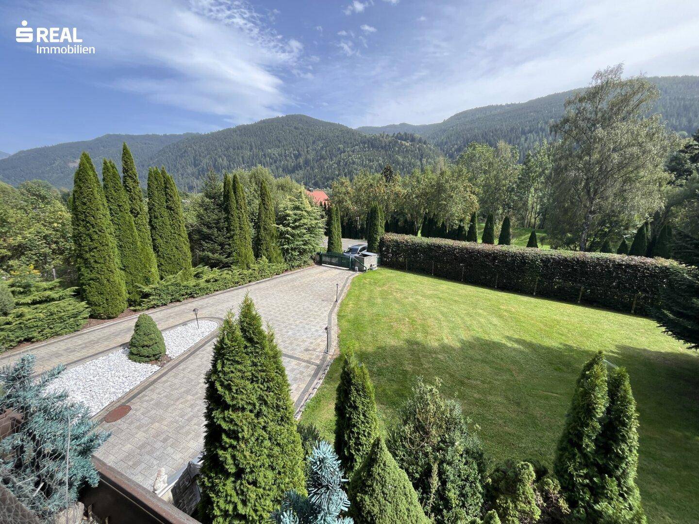 Panoramablick auf das Anwesen mit weitläufiger Auffahrt, gepflegtem Garten und umliegender Berglandschaft.
