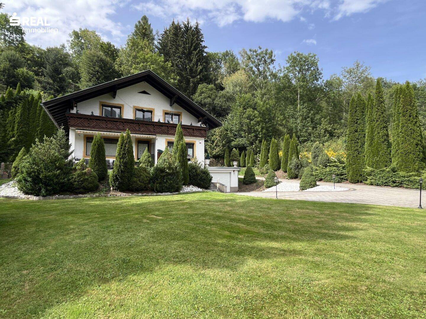 Einladendes Haus mit weitläufigem Rasen und gepflegten Hecken, eingebettet in eine grüne Hügellandschaft.
