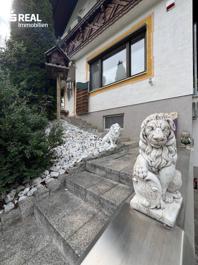 Eingangsbereich des Hauses mit Steintreppe, dekorativen Löwenstatuen und üppiger Bepflanzung.