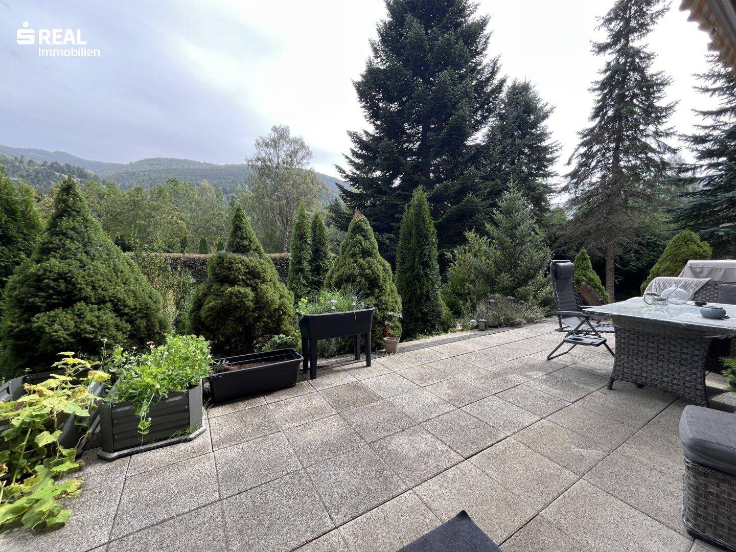 Gemütliche Terrasse mit Sitzgelegenheiten und Blick auf den grünen Garten und die umliegenden Hügel.