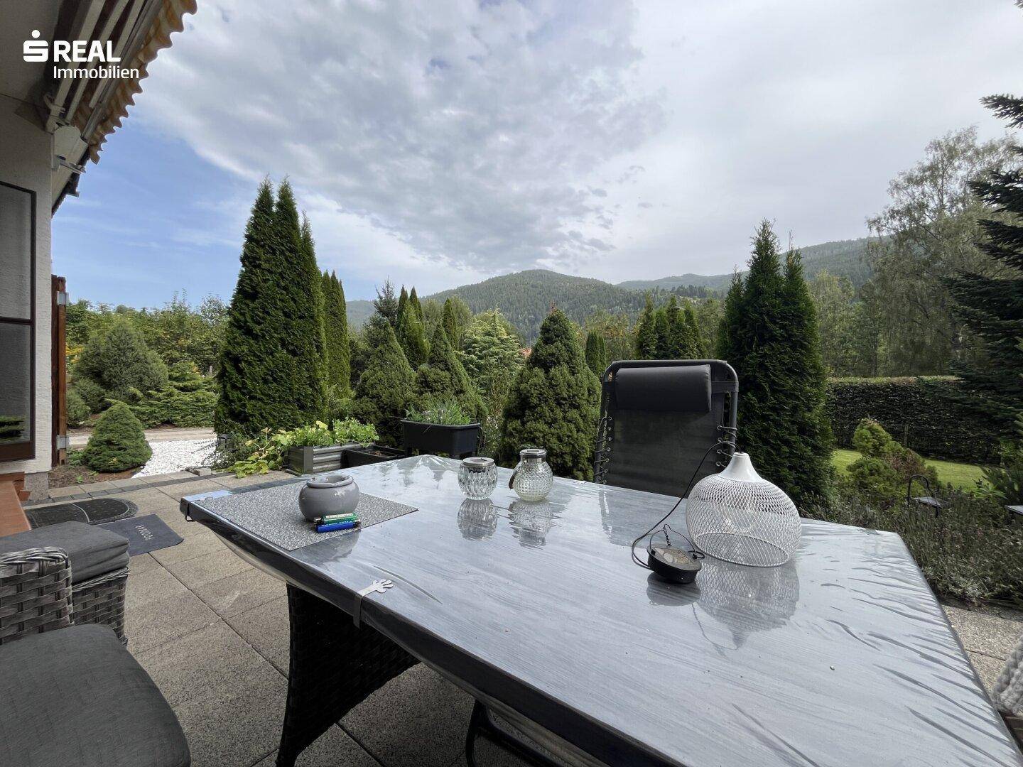 Einladende Terrasse mit Esstisch und Blick auf die grüne Landschaft und die bewaldeten Hügel.