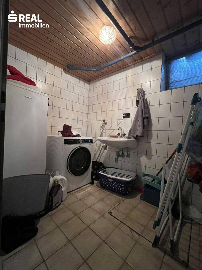 Praktischer Hauswirtschaftsraum im Keller mit Waschmaschine, Spülbecken und Holzdecke.