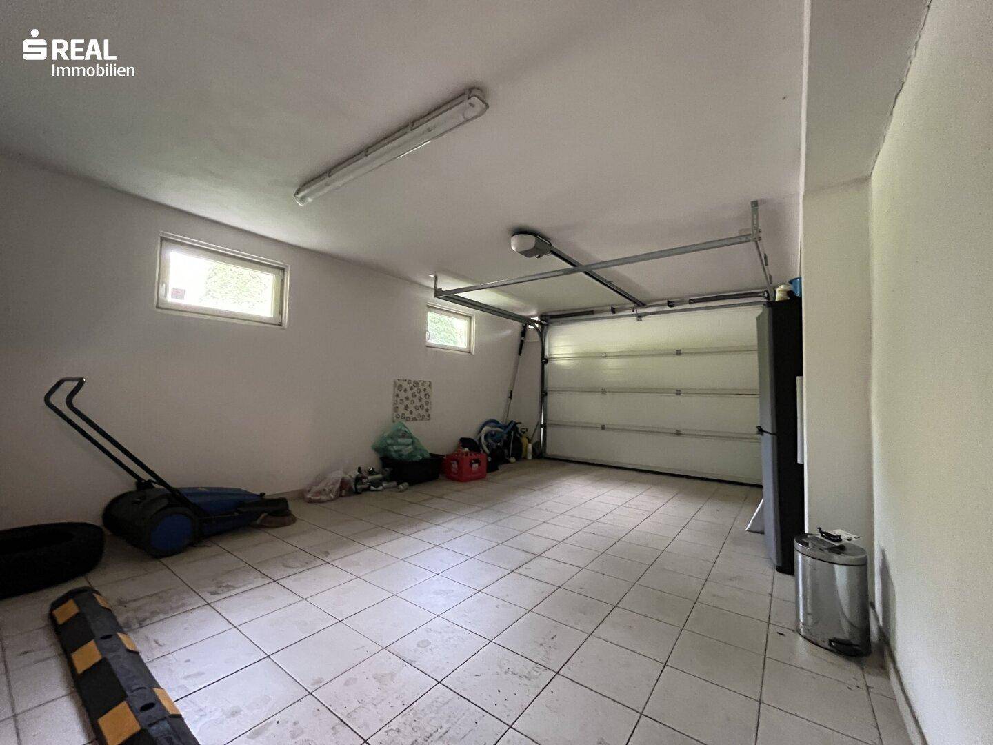 Geräumige Garage mit Rolltor, zwei Fenstern und gefliestem Boden.
